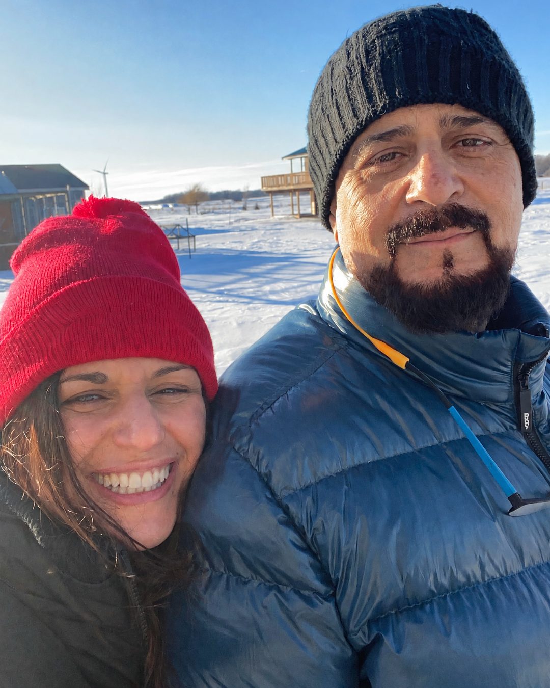 Brenda and Asim smiling together in hats and winter coats on the snowy land at A&B Healing