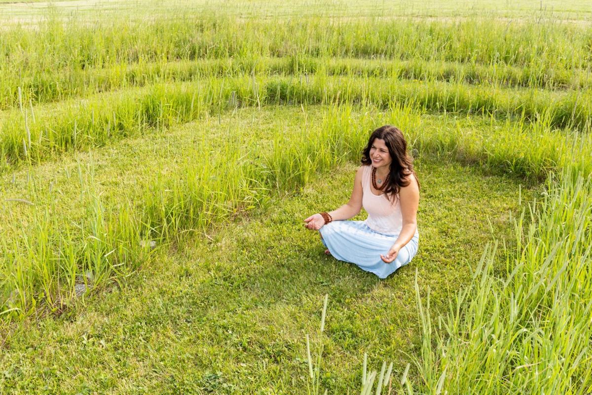 Brenda smiling as she sits in meditation inside the grass labyrinth at A&B Healing